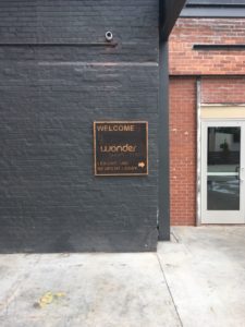 A rustic looking plaque on a dark brick wall that reads "Welcome - Wonder - Shops - Flats"